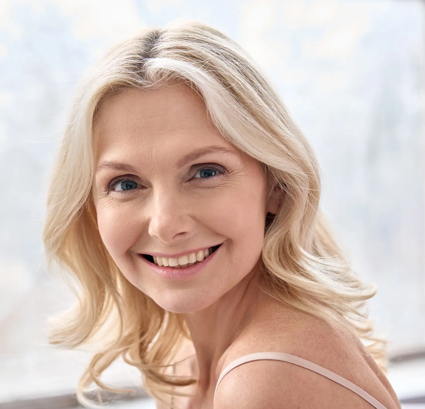 Happy mature elder 50s woman indoors. Closeup headshot portrait of attractive mid age woman looking smiling at camera. Beauty, skin care